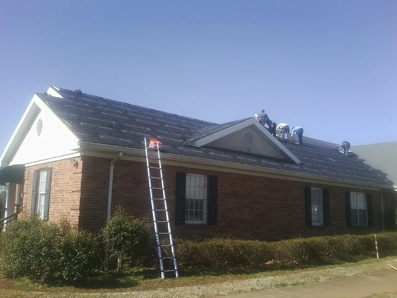 Crew tearing shingles off a brick ranch roof with a ladder set — Metal Roof Repair work by our crew in Oxford
