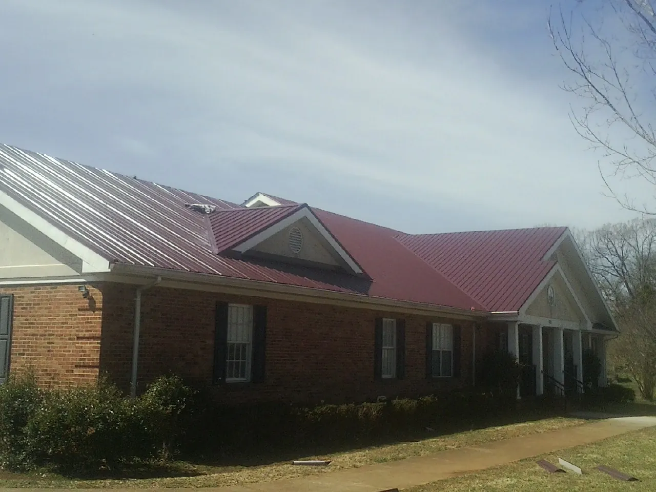 Red metal roof with gabled entries on a long brick building, from a Hail Damage Roof Repair job in Oxford